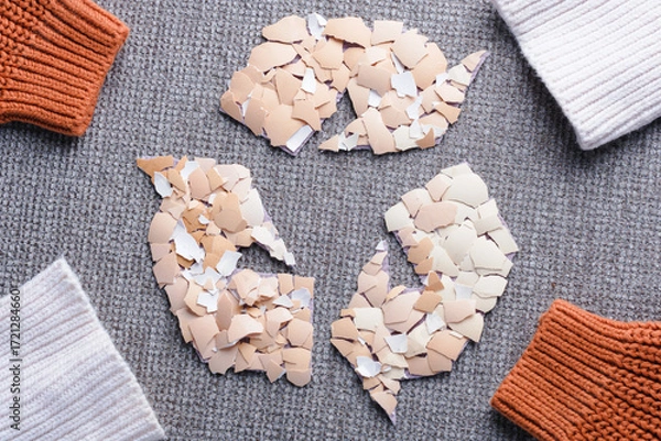 Fototapeta Creative recycling symbol with broken eggshell pieces surrounded by knitted sleeves in a circle on a gray textured surface. Use of eggshells in the textile industry as a sustainable material.  