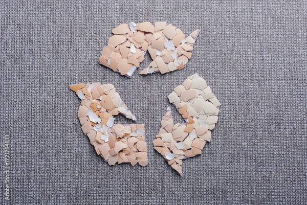 Fototapeta Creative recycling symbol with broken eggshell pieces surrounded by knitted sleeves in a circle on a gray textured surface. Use of eggshells in the textile industry as a sustainable material. top view
