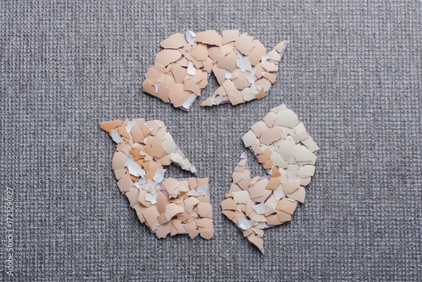 Fototapeta Creative recycling symbol with broken eggshell pieces on a gray textured surface. Use of eggshells in the textile industry as a sustainable material. Organic textile innovation. top view