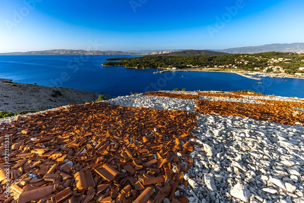 Fototapeta Rab the hill above the port in Lopar, the Croatian flag placed on a slope of red roof tiles,