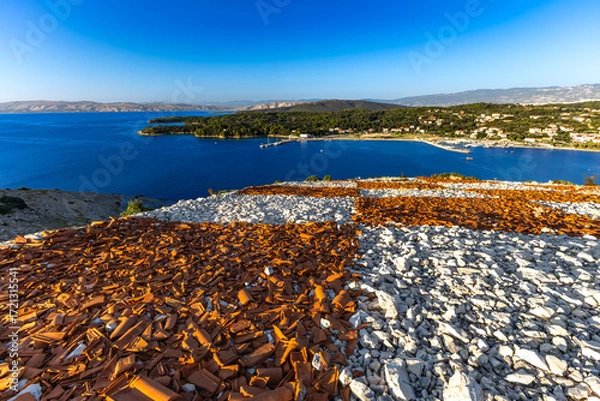 Fototapeta Rab the hill above the port in Lopar, the Croatian flag placed on a slope of red roof tiles,