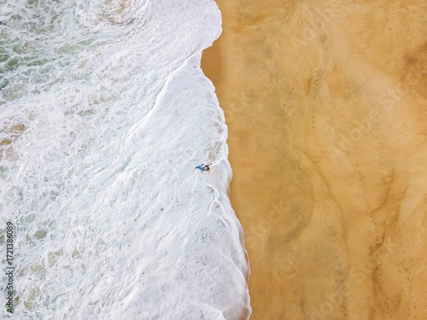 Fototapeta Aerial View of Surfer with Surfboard Walking Along Sandy Beach in Nazare, Portugal