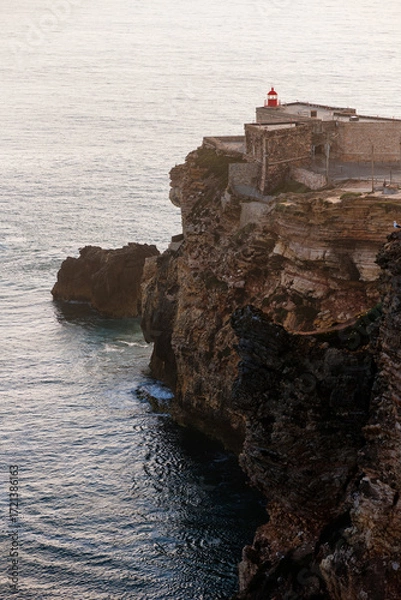 Fototapeta Lighthouse at Nazare’s Cliff-Edge Overlooking Atlantic Ocean, Waves Crashing and Dramatic Coastal Panorama in Portugal