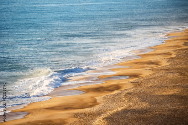 Fototapeta Golden Sandy Beach with Rolling Atlantic Ocean Waves in Nazare, Portugal, Famous Surf Destination