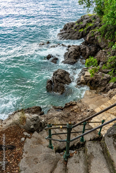 Fototapeta Rocky seaside with turquoise waves and stone steps leading to the ocean Lungomare Opatija Croatia