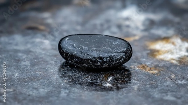 Fototapeta A black pebble on a wet surface.