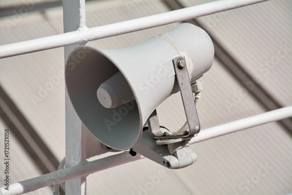 Fototapeta Close up of a passenger safety megaphone mounted on a white cruise ship railing. The equipment is crucial for announcing alerts and important messages.