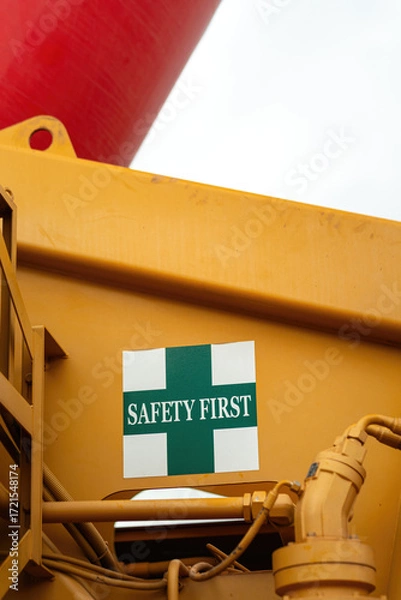 Fototapeta "Safety first" warning sign on the crane vehicle or industrial machine part. Safe working practice with risk condition. Close-up with selective focus.