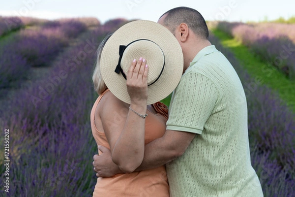 Fototapeta Couple embracing in lavender field, woman's face hidden by hat.