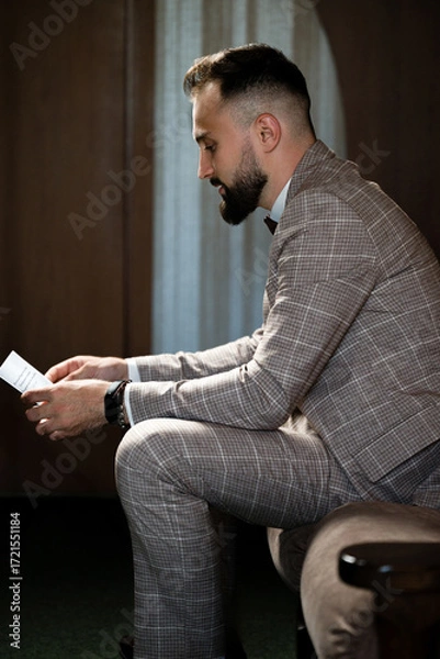 Fototapeta Man in suit reads a note, seated thoughtfully. A moment of contemplation.