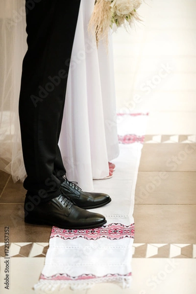 Fototapeta A couple's feet stand on a patterned aisle runner during a ceremony.