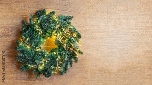 Fototapeta Christmas Background with Cozy Christmas wreath made of  fir tree branches and lights garland on a wooden surface. Christmas decorations. Copyspace