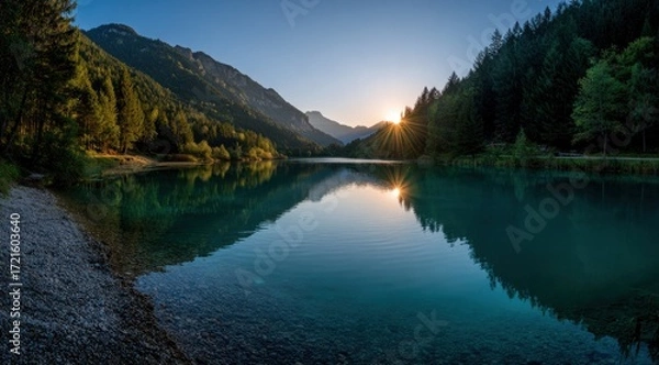 Fototapeta A serene lake reflecting a vibrant sunrise over towering mountains and lush forests, showcasing a tranquil and peaceful scene.