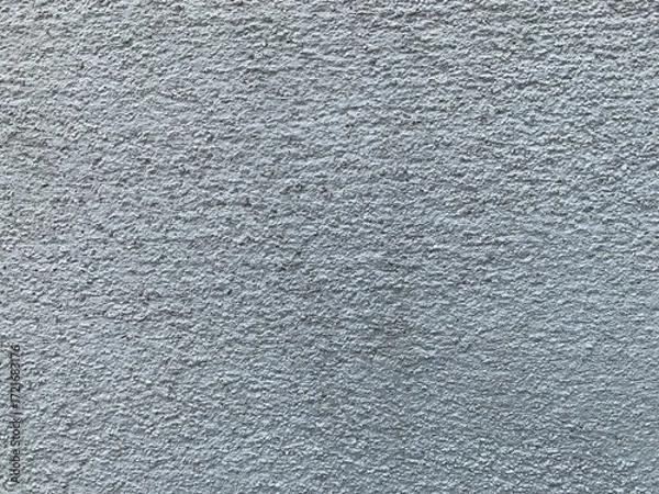 Fototapeta A close-up texture shot of a rough, light gray or blue stucco wall with a heavily grainy and bumpy surface.