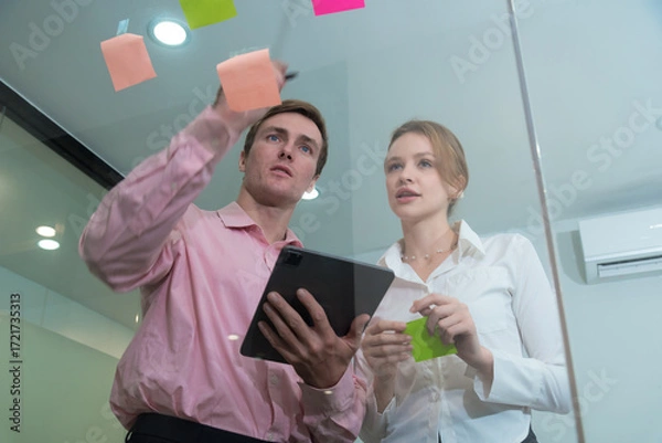 Fototapeta Creative professionals collaborate in modern office, using colorful sticky notes for brainstorming and planning. Their focused expressions reflect teamwork and innovation.