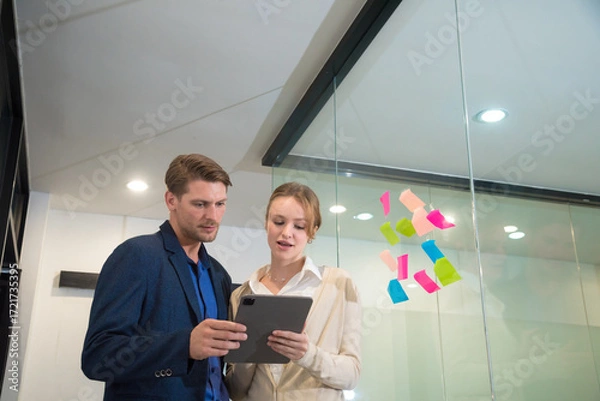 Fototapeta Efficient business meeting in modern office professional couple discussing project clipboard sticky notes teamwork collaboration corporate environment communication planning strategy.