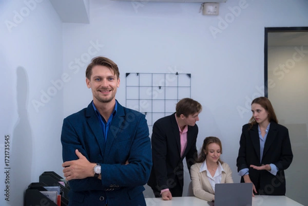 Fototapeta Professional group in office setting, showcasing teamwork and collaboration. man in blue suit gives thumbs up, while colleagues engage with laptop, reflecting positive work environment.