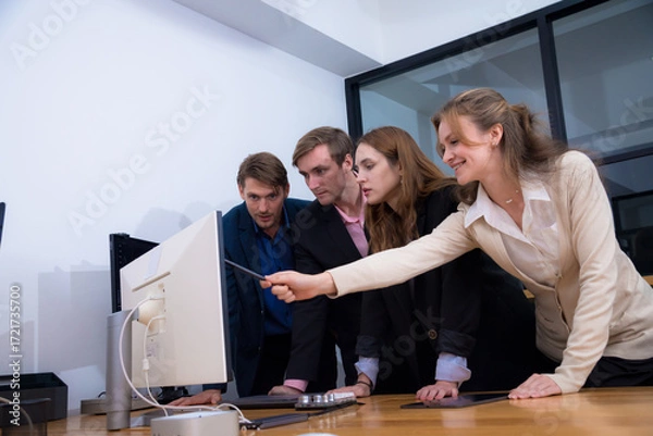 Fototapeta Collaborative team meeting in modern office, focused on computer screen. Four professionals, dressed in business attire, engage in discussion, showcasing teamwork and communication