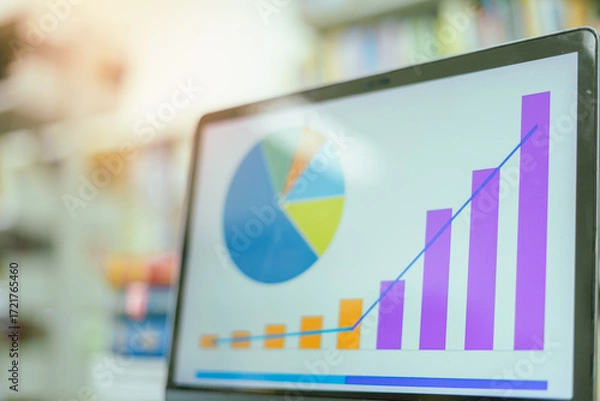 Fototapeta A laptop screen displaying a graph and a book placed on the table in the library, representing a business concept.	