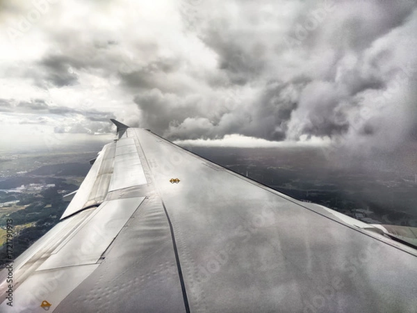 Fototapeta Cloudy skies create a dramatic view from an airplane wing during flight above a landscape