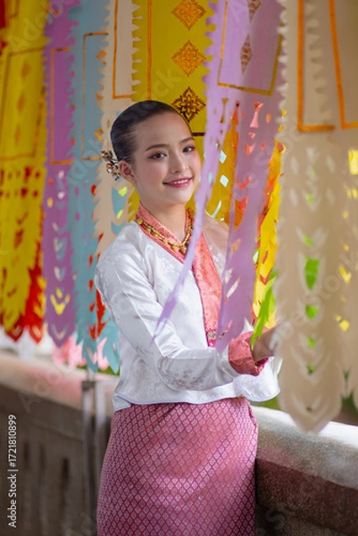 Fototapeta Woman in traditional attire smiles while standing beside colorful paper decorations, creating festive atmosphere