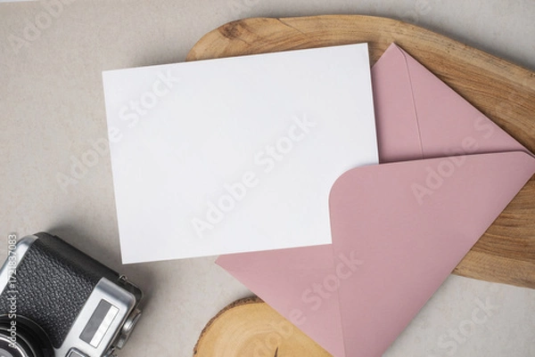 Fototapeta Empty white blank greeting or invitation card, envelope, vintage camera and wooden decoration on beige background.