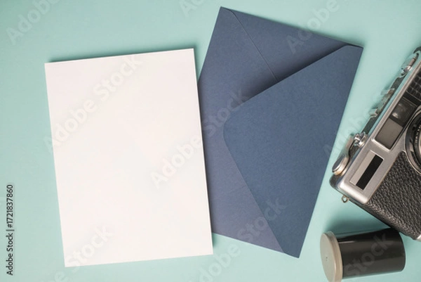 Fototapeta Empty white blank greeting or invitation card, envelope, vintage camera and film box on blue background.