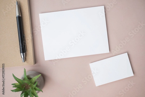 Fototapeta Empty white blank greeting or invitation card, name card, pen, note book, cactus on beige background.