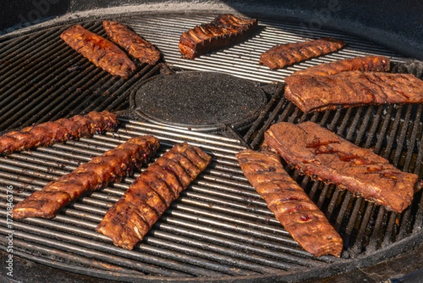 Obraz Grilled ribs cooking on round barbecue grill. Delicious barbecue pork ribs with crispy dry rub seasoning placed on circular grill ready for serving.