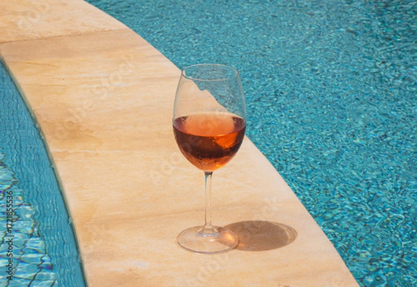 Fototapeta Glass of chilled rosé wine on poolside edge, summer refreshment under bright sunlight,