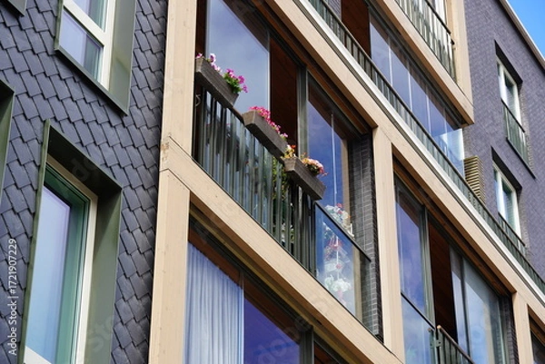 Fototapeta Modern apartment building with balconies featuring colorful flowers in a vibrant urban setting during daylight hours