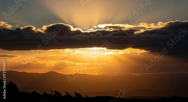 Fototapeta Golden Rays of Light Shine Through Dramatic Clouds Over Mountain Landscape