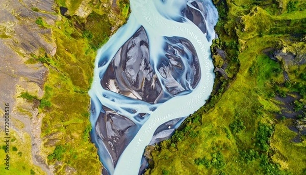 Fototapeta Aerial view of a glacial river's intricate path carving through vibrant green and black landscape
