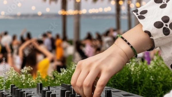 Fototapeta A female DJ mixes music at an outdoor beach party with a blurred crowd dancing in the background