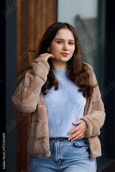 Fototapeta A girl in blue jeans and a warm jacket against the background of a bench.