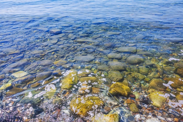 Fototapeta Colorful stones in transparent water on background of clear blue Aegean Sea with small surface waves. Greece.