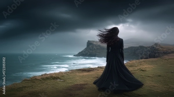 Fototapeta Woman stands on a grassy hill overlooking the ocean. The sky is dark and stormy. Scene is somber and melancholic