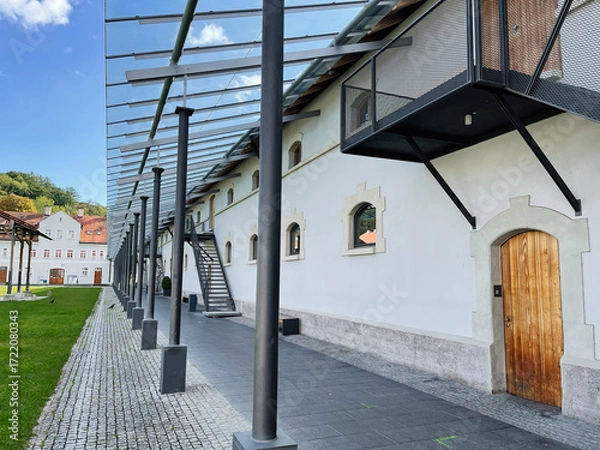 Fototapeta Modern white building with arched windows and wooden door under a metal canopy in Furstenfeldbruck, Germany