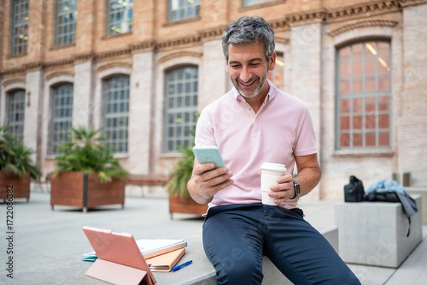 Fototapeta Smiling man using smartphone taking coffee break outdoors
