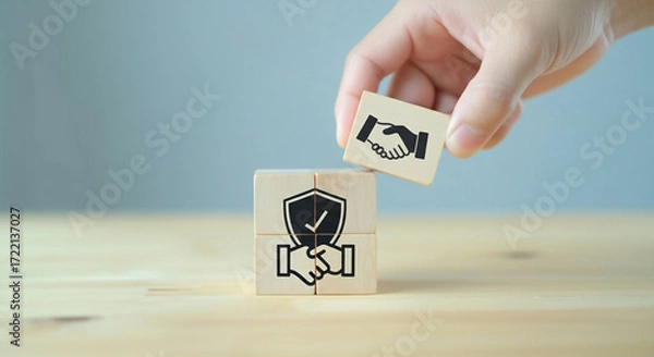 Fototapeta A person is building a structure with blocks featuring a handshake and a security shield, conveying the concept of a secure collaboration.