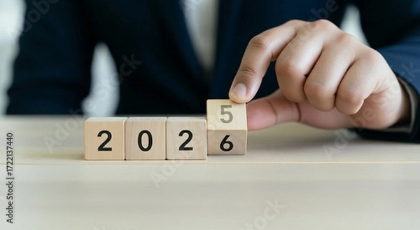 Fototapeta A person is shown completing the year "2026" with wooden blocks, representing a new business cycle, goal achievement, and time progression.