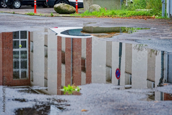 Fototapeta Puddle mirrors a home and a two way no parking sign