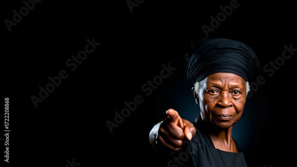 Fototapeta Elderly African Woman in a Headwrap Pointing Forward. Strong Matriarch, Wise Elder, Direct Command.