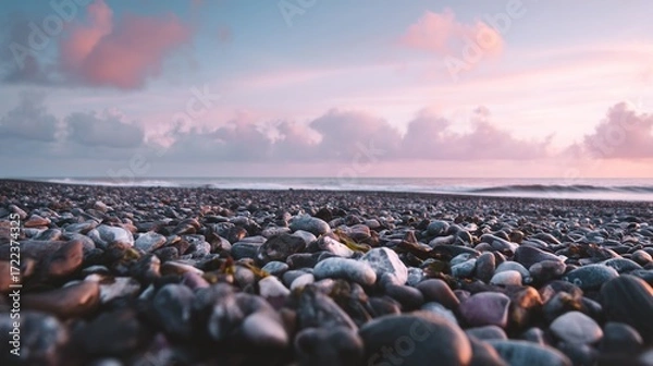 Fototapeta The beautiful sunrise over the sea, with pebbles in the foreground in front of the camera, captures a cinematic scene, and the sky along with the shallow depth of field creates a surreal effect.