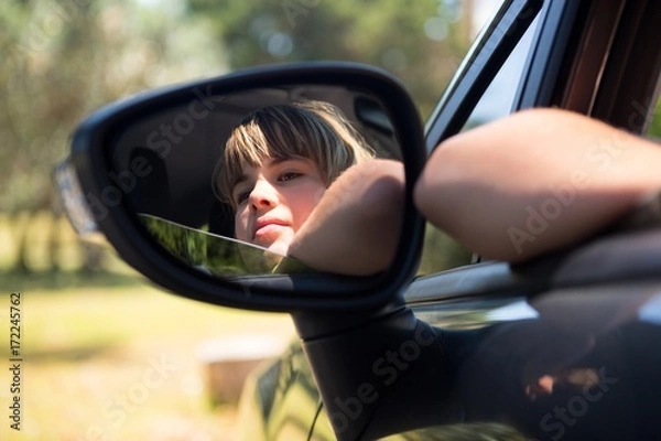 Fototapeta Reflection of teenage girl in wing mirror of a car