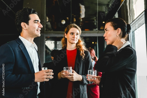 Fototapeta Three professionals in formal attire network at corporate reception, chatting with drinks. Event scene includes sales, partnership, seminar vibes, collaboration, planning, and new opportunities.