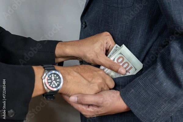 Fototapeta An illicit transaction taking place between two business professionals. One man is discreetly slipping a wad of cash into the inner pocket of another person's suit, symbolizing bribery and unethical b