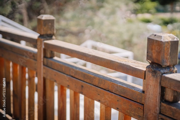 Fototapeta Close-up of a sunlit wooden railing with a natural, rustic finish. The background is softly blurred, highlighting the texture and detail of the wood.
