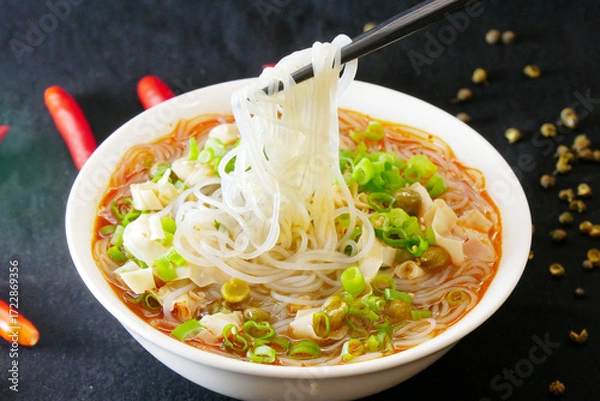 Obraz Close-up of a person picking up rice noodles with chopsticks, depth of field