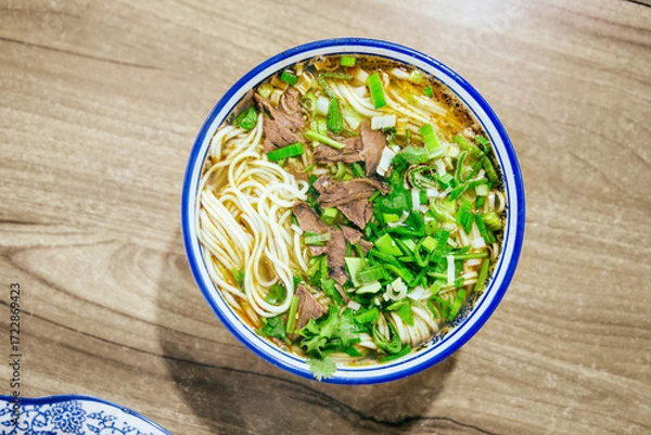 Obraz Close-up beef noodle with clear soup on wooden table, minced garlic, beef slices